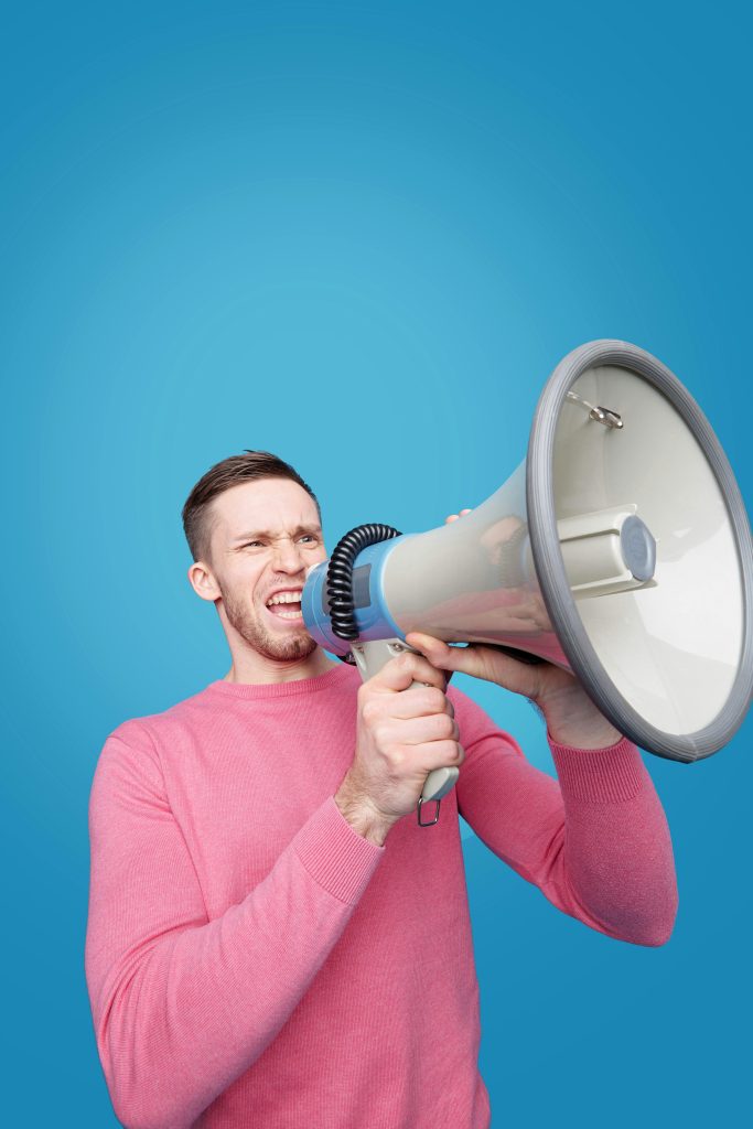 Dynamic image of a man energetically shouting into a megaphone with vibrant blue background and expression of emotion.
